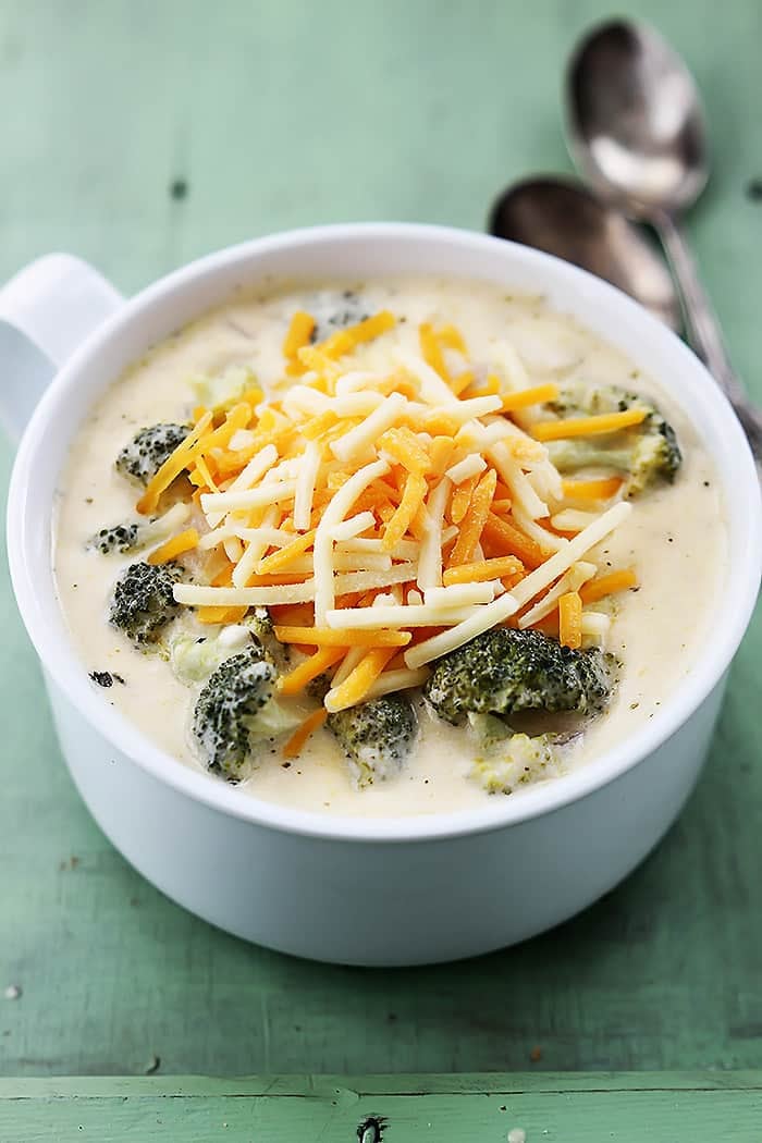 slow cooker broccoli cheese soup in a bowl with spoons on the side.
